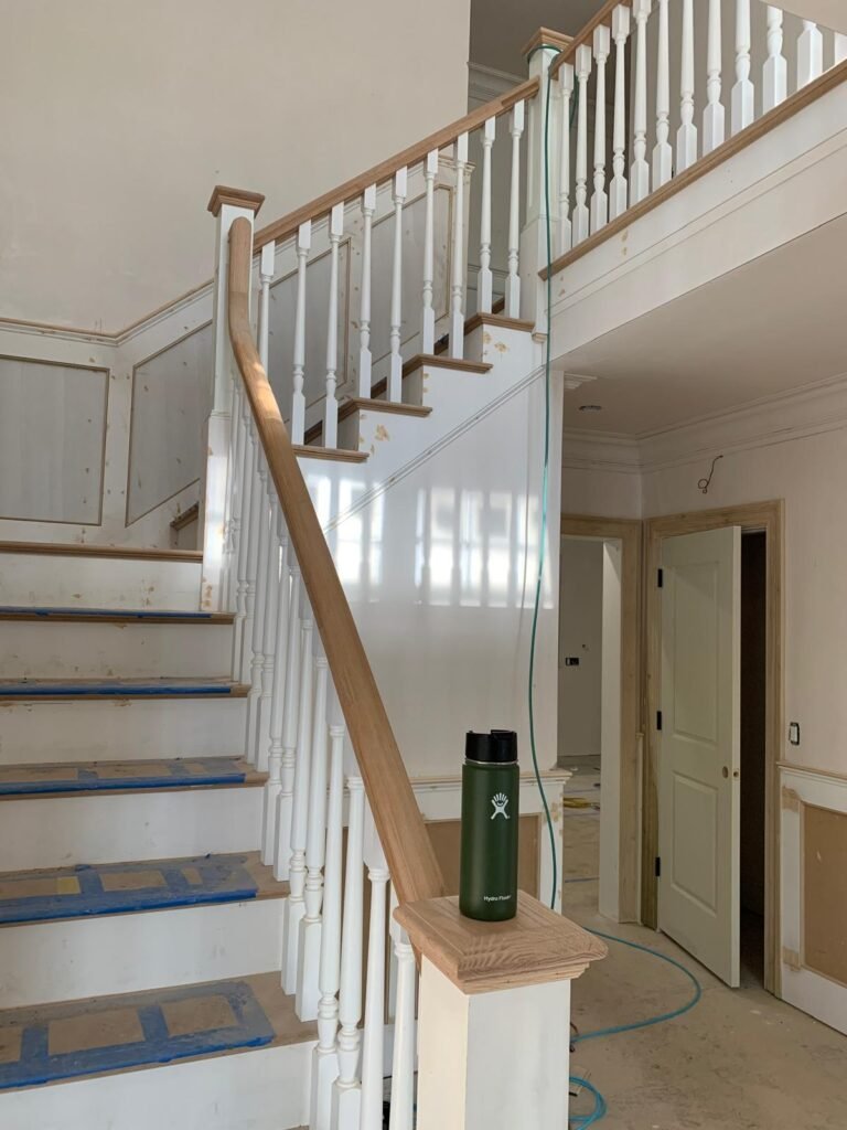 Staircase with oak handrail and white balusters by WHB Construction Corp.